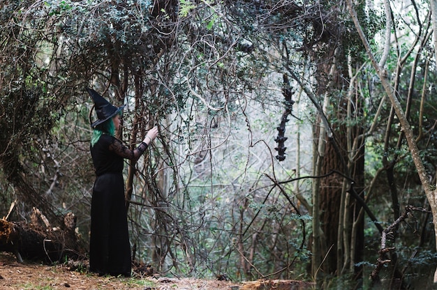 Young witch looking at mysterious forest arch