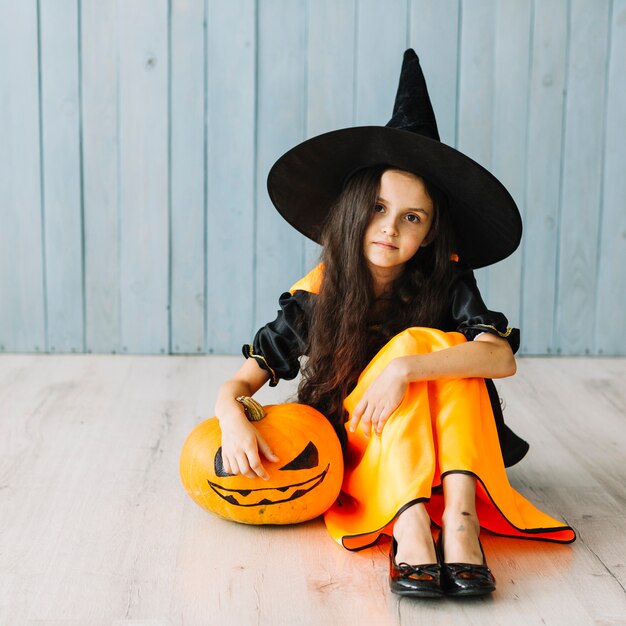 Young witch sitting with pumpkin on Halloween party