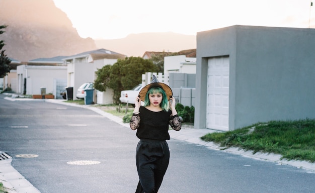 Young witch on suburban street holding hat