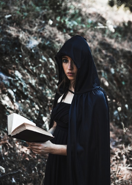 Free photo young witch with book in thicket