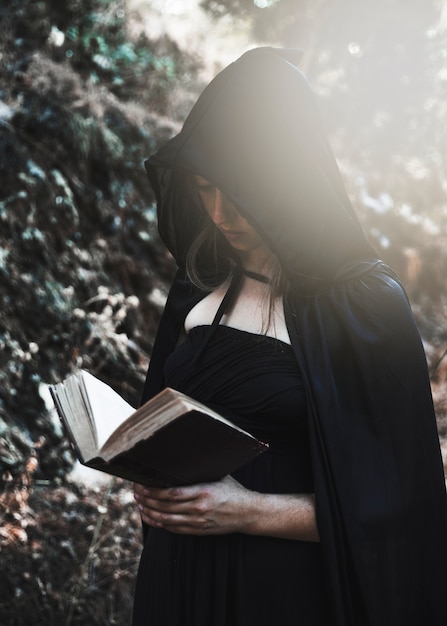 Бесплатное фото Молодая ведьма с открытой книгой в солнечной чащи