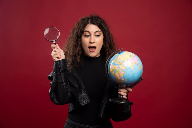 Free photo young woman in all black outfit holding a globe with loupe.