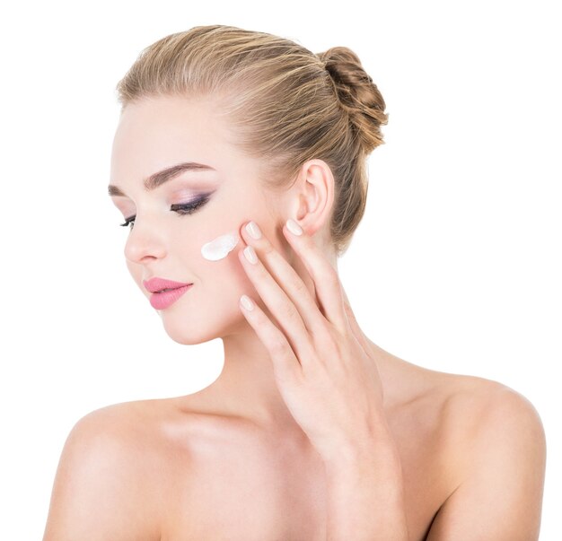 Young woman applies cosmetic cream on a face.