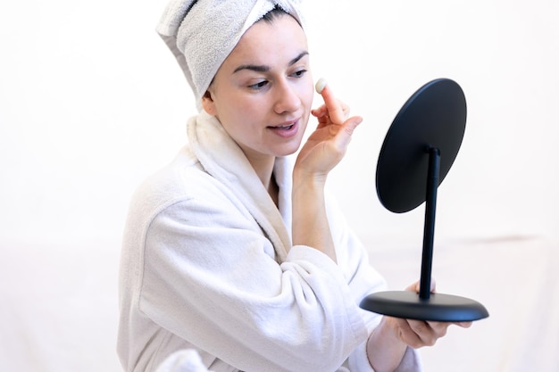 A young woman applies cream on her face looks in the mirror