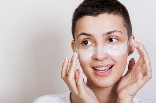 Free photo young woman applying face cream