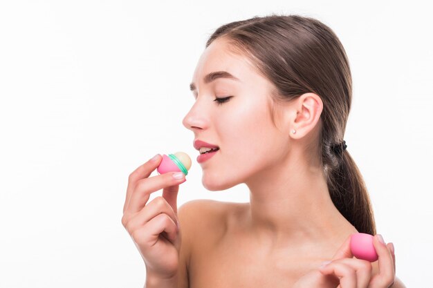Young woman applying hygienic lip balm on white wall