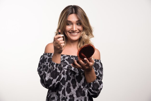 Young woman applying lipstick with happy expression.