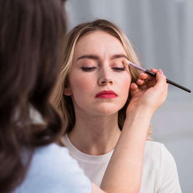 Young woman applying makeup by visage artist