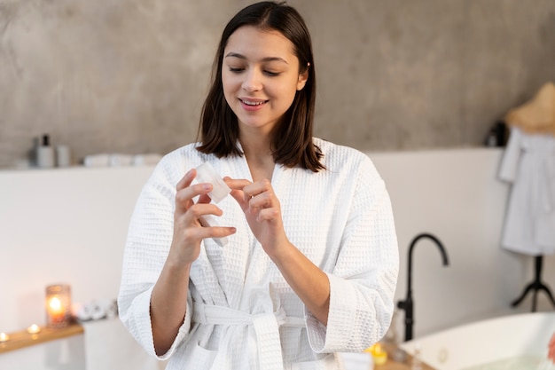 young woman applying moisturizer on her face before taking a bath