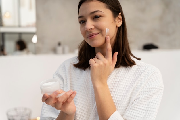 Молодая женщина наносит увлажняющий крем на лицо перед принятием ванны