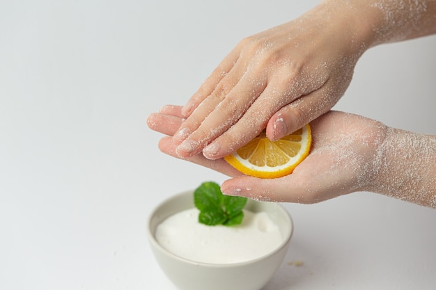 Young woman applying natural lemon scrub on hands against white surface