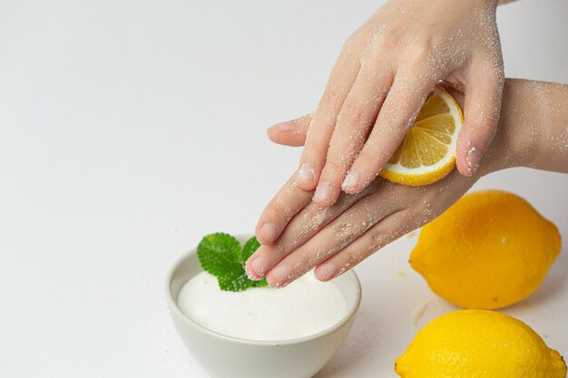 Young woman applying natural lemon scrub on hands against white surface