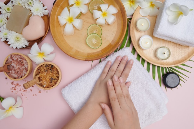 Young woman applying natural scrub on hands against pink surface. Spa treatment and product for female hand spa, massage, perfumed flowers water and candles, Relaxation. Flat lay. top view.