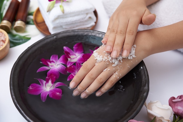 Young woman applying natural scrub on hands against white surface. Spa treatment and product for female hand spa, massage, perfumed flowers water and candles, Relaxation. Flat lay. top view.