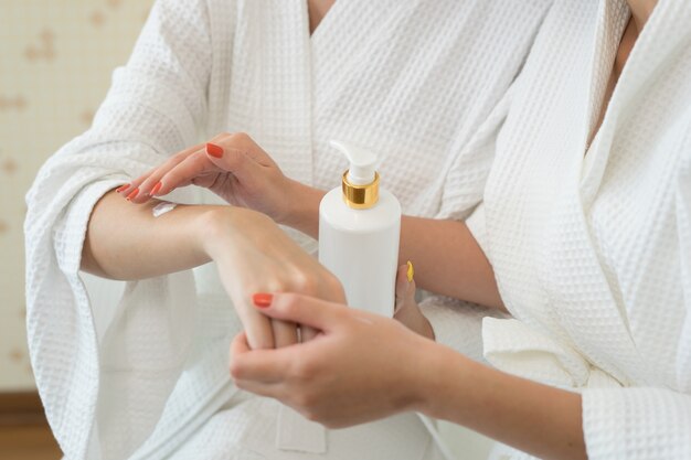 Young woman applying with finger white moisturizing cream on hand.