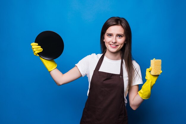 洗った皿を見てスポンジとエプロンの若い女性。きれいな皿、家での注文は大変な作業です。完璧な主婦はランクに値する