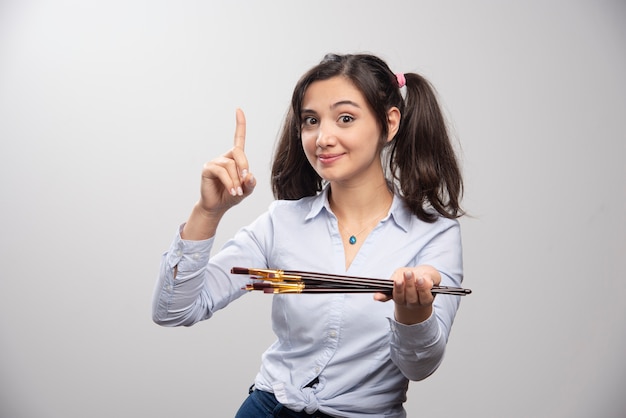 Young woman artist holding paintbrushes on gray wall. High quality illustration