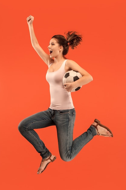 점프 하 고 빨간색 배경에 스튜디오에서 공을 차는 축구 축구 선수로 젊은 여자.