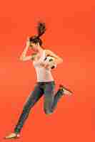 Free photo the young woman as soccer football player jumping and kicking the ball at studio on a red background.