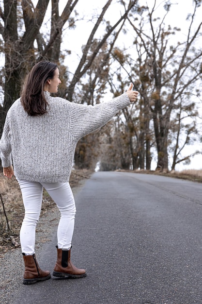 Free photo young woman on asphalt road hitchhiking concept