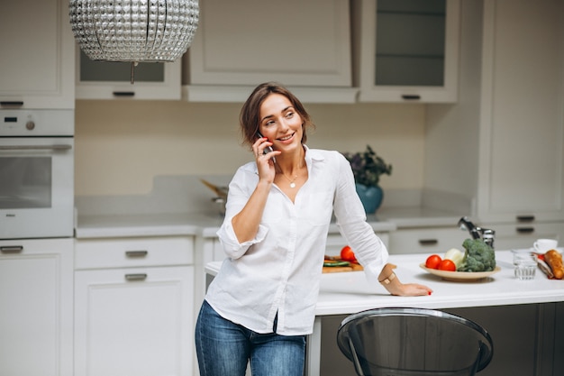 Бесплатное фото Молодая женщина на кухне приготовления завтрака и разговаривает по телефону