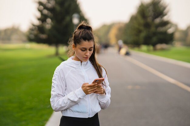 Young woman athlete holds and uses smartphone after jogging
