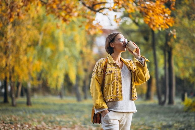 コーヒーを飲みながら秋の公園で若い女性