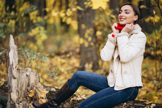 Giovane donna in un parco in autunno seduto su un tronco