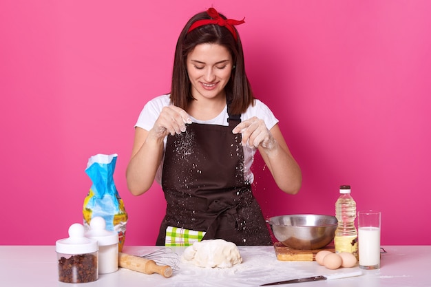 Free photo young woman baker in kitchen, sprinkling white flour on dough, baking delicious coockies, likes homemade pastry, posing isolated on pink. copy space for your advertismant or promotion.