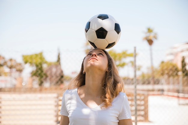 Молодая женщина, балансируя футбольный мяч на голове