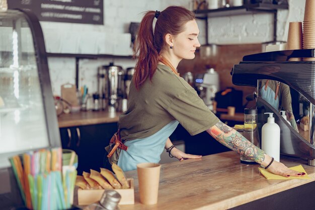 Молодая женщина-бариста убирает прилавок в кафе