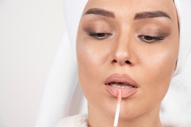 Young woman in a bathrobe applying a lipstick .