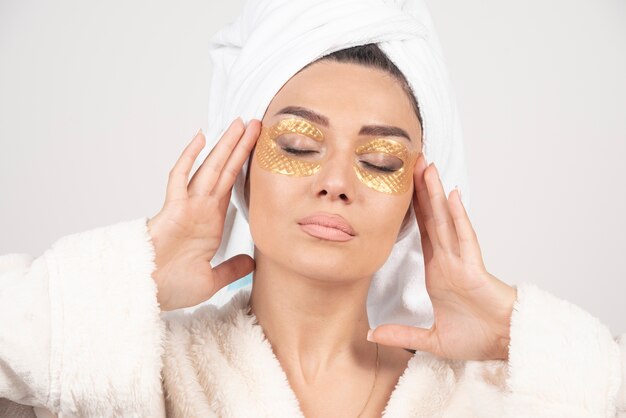 Young woman in bathrobe and cosmetic eye patches posing .