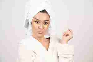Free photo young woman in bathrobe and cosmetic eye patches posing .