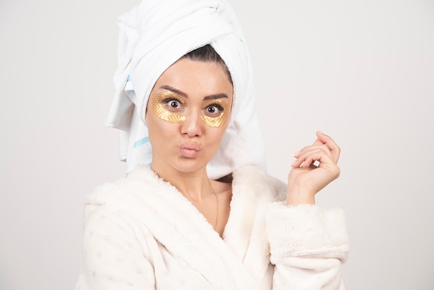 Young woman in bathrobe and cosmetic eye patches posing .