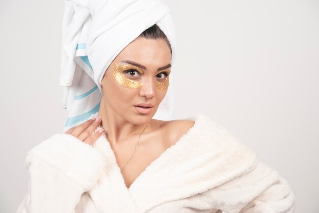 Young woman in bathrobe and cosmetic eye patches posing .