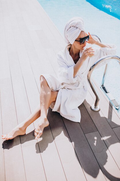 Young woman in bathrobe drinking coffee by the pool