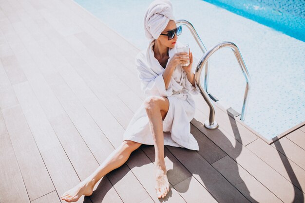 Free photo young woman in bathrobe drinking coffee by the pool