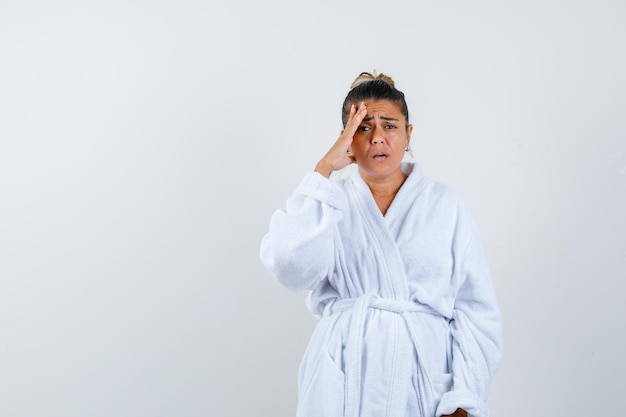 Free photo young woman in bathrobe holding hand on forehead and looking forgetful