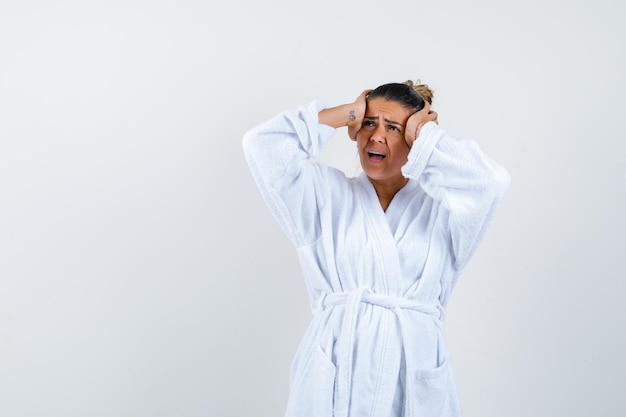 Young woman in bathrobe holding hands on head and looking annoyed