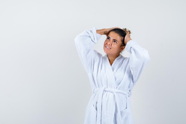 Young woman in bathrobe holding hands on head and looking wondered