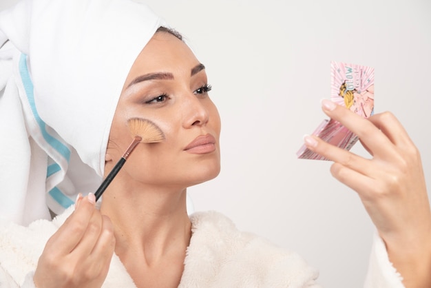 Young woman in a bathrobe holding make-up brush .