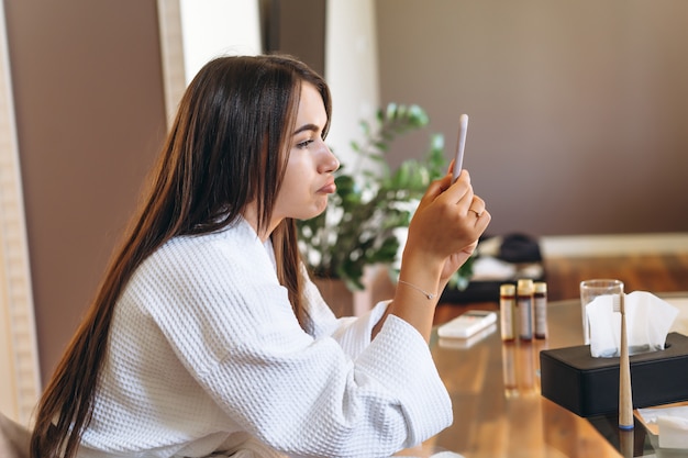 携帯電話を使用してホテルの部屋でバスローブの若い女性