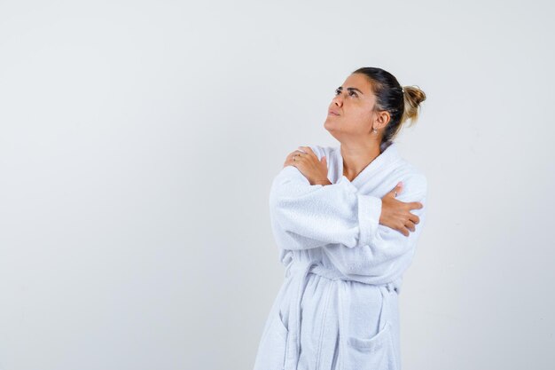 Young woman in bathrobe hugging herself and looking cute