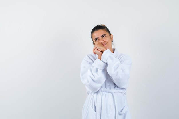 Young woman in bathrobe leaning cheek on hands and looking pensive