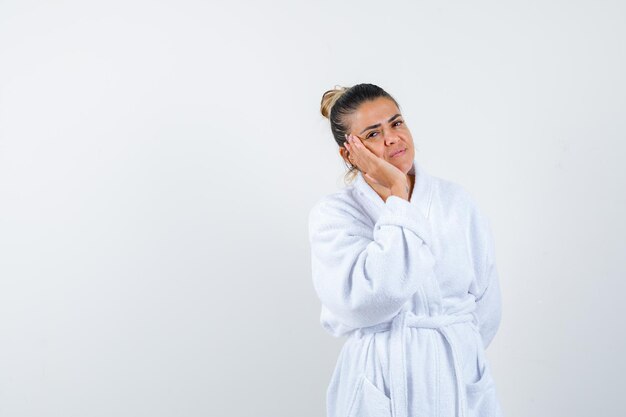 Young woman in bathrobe leaning chin on hand and looking wistful