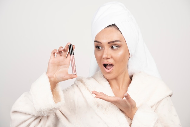 Young woman in a bathrobe looking at lipstick .