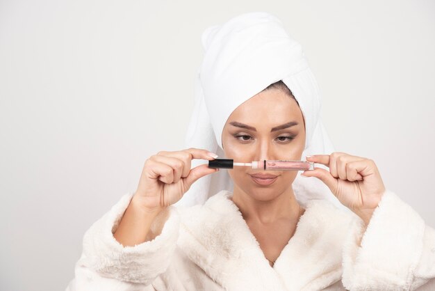 Young woman in a bathrobe opening a lipstick .