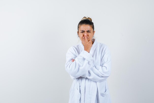 Young woman in bathrobe pressing nose with finger and looking funny