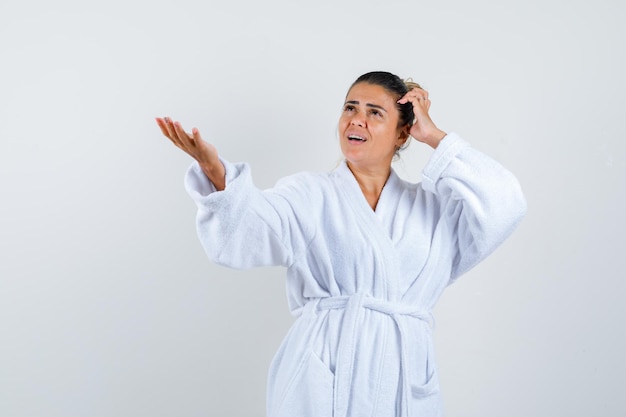 Young woman in bathrobe pretending to show something and looking confident